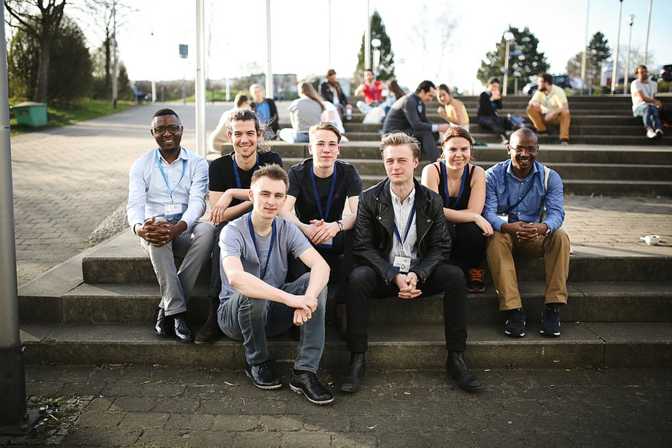 Group picture of 7 team members of the Conference 2018 who are sitting ion the steps in front of the University 