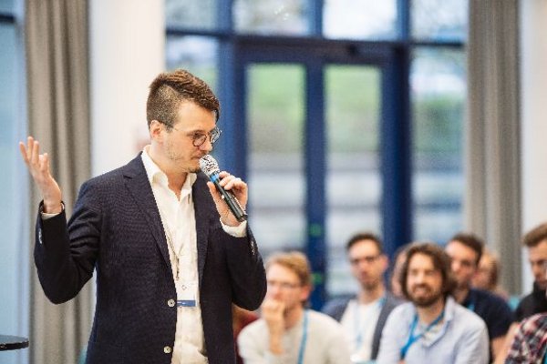 A male lecturer is talking into a microphone in front of the listening participants