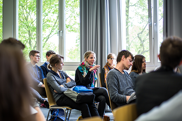 Participants sitting on chairs and listening to a female student thet is posing a question to the student presenting his paper 